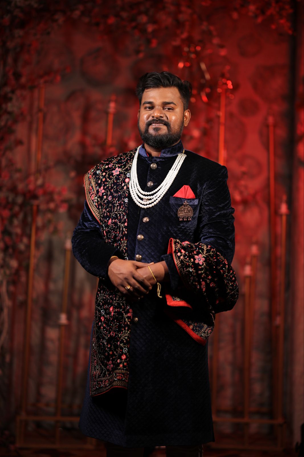 Groom portrait in dark attire against a red background